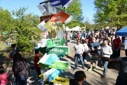 groups of people walking around a post with directional arrows pointing every direction, at the Dogwood Arts Festival