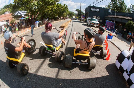 People race each other on adult big wheels in a friendly competition at the East Atlanta Strut, a fall festival