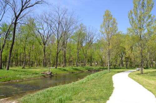 Paved Pedestrian Trail Follows Along A Winding Stream Through Woods