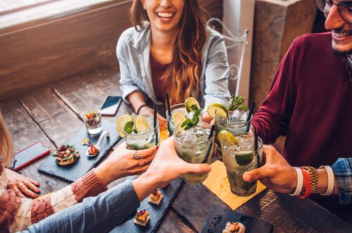 friends drinking mojitos at a bar, enjoying drinks and food at a trendy restaurant