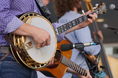 Close up of a banjo players hand as they are playing a live show. guitarist and stand up bassist in the back