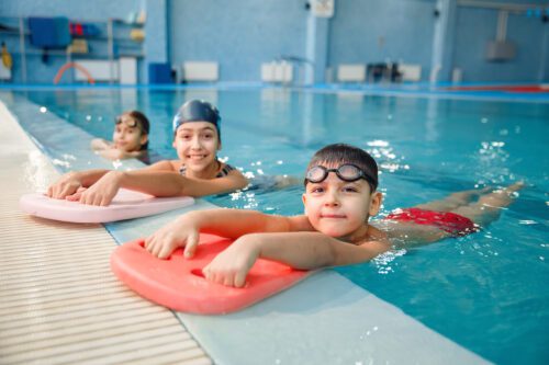 kids by the poolside taking a swimming lesson