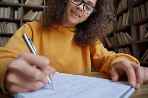 Happy teenage girl, in a yellow hoody, writing in a notebook