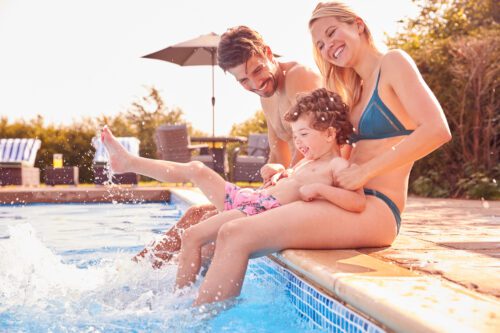 happy couple sitting on the pool edge with their young son.