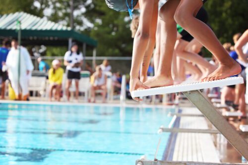 rows of swimmers on starting blocks ready to jump into the water at a swim meet