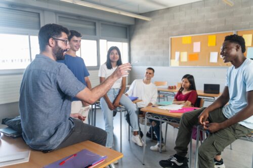 Teacher casually explaining the lesson to a group of students circles around him