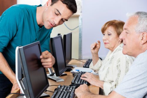 group of seniors in a technology course for computer literacy, with younger instructor helping them.