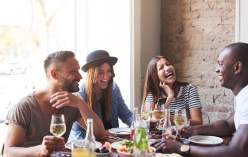 diverse group of friends, laughing and drinking while enjoying trendy dinner