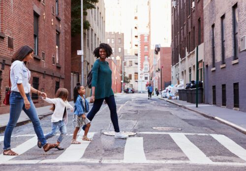 Two mother friends walking across the street with their children